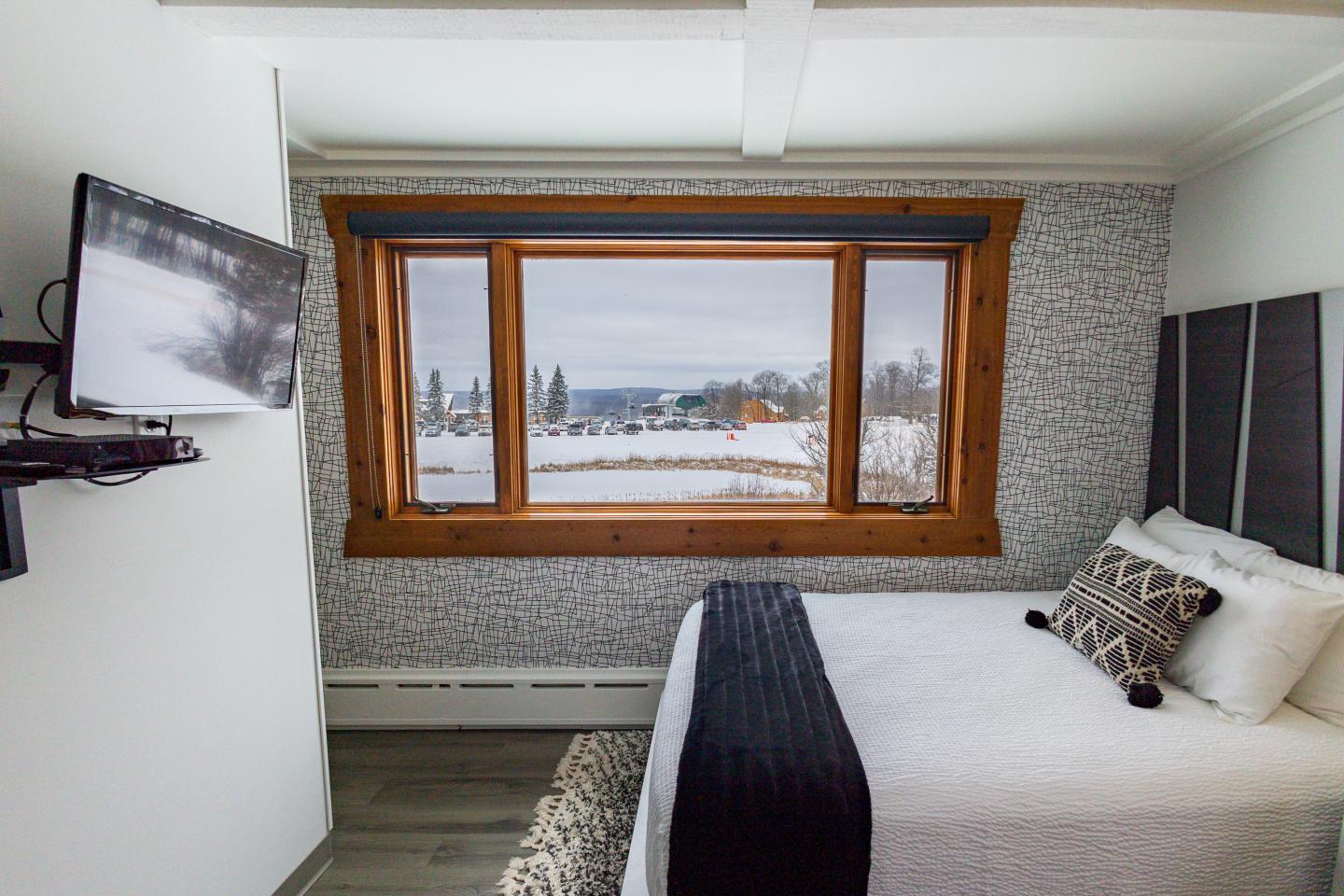 Queen bed near window with chairlift and ski slope just outside.