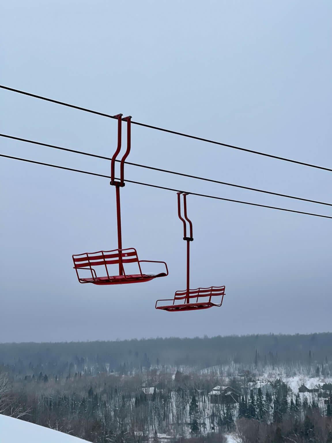 Two quad chairs hang from a cable with cloudy skies in the background.
